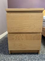 Front view of two-drawer wooden cabinet showing natural wood finish and drawer fronts.