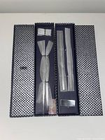 Box containing two pairs of black and silver chopsticks and two chopstick holders arranged inside patterned packaging.