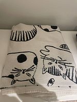 Folded cream blanket with black outlined cat faces and stripes pattern