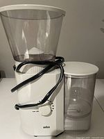 Front view of white Braun coffee grinder with black power cord wrapped, clear hopper on top with lid, dial on front.