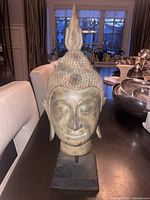 Front angle view of the brass Buddha head sculpture showing facial details and flame finial.