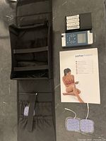 Full kit laid out including carrying case, electrodes with wires, manual, and stimulator device with batteries