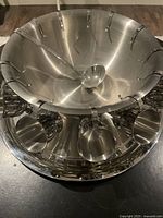 Top and angled view showing the large punch bowl with 12 matching cups hanging from hooks around the rim. Ladle resting inside the bowl.