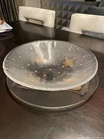 Clear glass decorative plate showing gold dot and star pattern, shallow bowl shape on dark surface with basic room background.