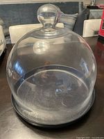 Clear glass dome cover with knob handle on top, placed on a table.