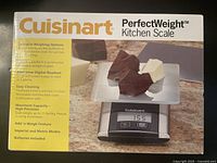 Front display of Cuisinart PerfectWeight kitchen scale box with image of scale and features: dishwasher-safe stainless steel cover, easy-clean touchpad buttons, max 11 lbs/5 kg capacity, LCD display, batteries included.