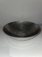 Side view showing the circular hammered metal bowl in silver tone on a white surface.