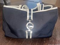 Front view of black fabric handbag with white trim and silver clasp detail on central white stripe