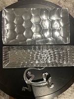 Two rectangular silver trays with distinct textured patterns on a dark round surface.