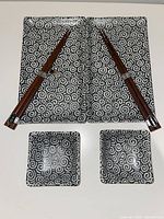 Two rectangular sushi plates, two small square dishes, and two pairs of chopsticks on a white background showing the swirl design and chopsticks