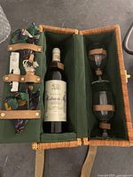 Open wicker basket showing two wine glasses and one wine bottle secured inside with leather straps against green fabric interior.