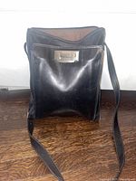 Front view of the black leather shoulder bag showing outer pocket with metallic clasp and adjustable strap