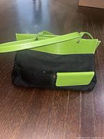 Side view of handbag showing black canvas body with green faux leather strap and pocket.
