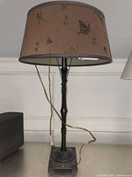 Full view of the large beige fabric lamp showing lampshade decorated with Chinese characters and insects and black tall lamp base.