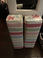 Two large fabric bolsters viewed from the side, showing multicolor horizontal stripes in pastel colors.