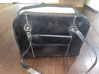 Front view of the black leather handbag showing stitching and front pocket