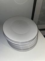 Stack of 10 white plastic plates from top view, showing flat surface and slightly raised edges.