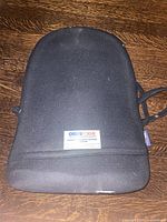 Front view of black ObusForme back support cushion on wooden floor showing label and shape.