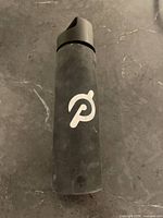 Front view of the black glass Peloton water bottle with silicone sleeve on a marble surface.