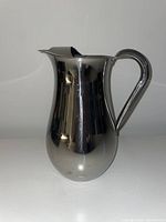 Side view of polished stainless steel pitcher showing shape, handle and spout.