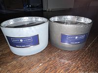 Two Scott Living scented candles in glass containers with speckled silver rims, shown from the side. One labeled "Garden Party" and the other "House Warming".