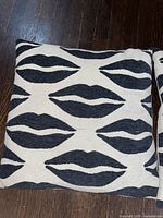 Single cream-colored throw pillow with black lips design on a dark wood floor