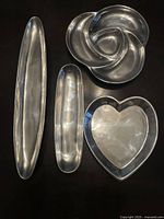All four decorative pans displayed on a flat surface, showing their different shapes and sizes: heart, flower swirl, medium oval, and narrow oval.