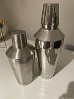 Side view of two stainless steel cocktail shakers showing their polished exterior and fitted caps.