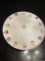 Top-down view showing colorful cupcake illustrations around the rim and a central cupcake with candle and text.