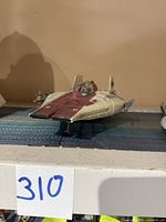 Side and front view of the 1997 Hasbro A-Wing Fighter toy showing beige and dark red paint with cockpit and figure inside.