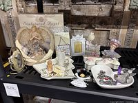 Photo of assorted angel-themed decor items including sculptured angel night light, porcelain music box, cross-shaped trinket dishes, porcelain picture frames, Mikasa Christmas tree dish, Virgin Mary sculpture, and San Francisco music box porcelain head.
