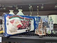 Boxed Sleeping Santa Animatronic Porcelain Doll with two Department 56 collectible village church models visible beside box.