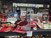 Overview of the assorted Christmas ornaments, tinsel, bows, candle, and wall art all arranged on a black shelf.