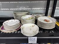Multiple stacks of assorted china plates and bowls on shelf showing varied patterns and sizes.