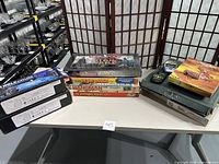 Photo of various boxed board games stacked on a white table, including Star Wars Monopoly, deluxe Scrabble, Hangman, Scavenger Hunt, and Solitaire.