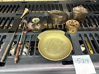 Seven brass items arranged on a plastic rack including cricket boxes, candle toppers, pocket change dish, and small trinket boxes