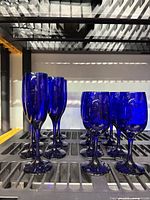 Seven cobalt blue champagne flutes and eight cobalt blue wine glasses displayed together, showing the overall lot contents and condition.