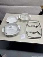 Three Corning Ware casserole dishes with glass lids and metal trivet on table
