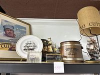 Framed promotional display including framed plate, two ship models, lamp with Cutty Sark 12 shade, and glass box with ship model on a shelf.