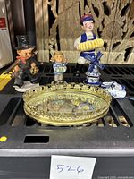 Group photo showing four porcelain figurines including two Goebel figurines, porcelain singing figurine, porcelain clogs, and the mirrored tray.