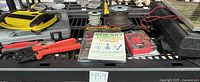 Electrical supplies laid out on a black grate shelf showing multimeter, wire cutters, small solar panel, and spools of wire