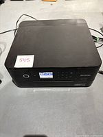 Full view of the black Epson XP-6100 printer showing the top and front with control panel and LCD screen, powered on with label number 545 placed on top.