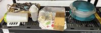 Wide photo showing all included kitchen items on shelf including Farberware cutting board, vintage Tupperware salt and pepper holder, utensils, mixing bowls with lids, containers, hand mixer, salad dressing bottle, and lemon juicer.