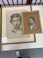Two framed pastel portraits placed side by side on white surface, woman portrait larger with silver metal frame and beige mat, girl portrait smaller with gold frame.