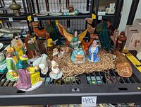 Full view of all hand-painted glazed pottery nativity figurines arranged on black metal shelf showing all figures including animals, angels, wise men, holy family with straw bedding