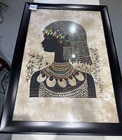 Framed beaded cloth artwork showing full view of the woman in side profile with colorful beadwork and black frame.