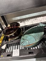 Photo showing the two items side by side on a black shelf: the fish baker and casserole on chafing stand