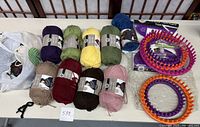Top-down view of two circular knitting looms, various skeins of yarn including dark purple, green, yellow, blue, taupe, maroon, brown, and pink on a table.