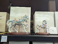 Two Lenox carousel horse figurines on a shelf with their original boxes behind, showing detailed pastel colors and wooden bases.