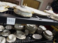 Shelved view showing multiple plates, bowls, and covered dishes with gold trim in the Haviland Limoges Cliver pattern.